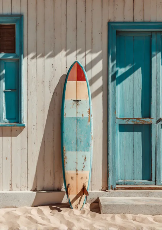 Vintage weathered striped surfboard in blue cream and coral red leaning against a whitewashed wooden beach shack with turquoise door and window on white sand with palm tree shadows